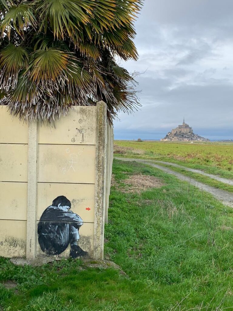 Boy crouched in the shadow of Mont Saint Michel.